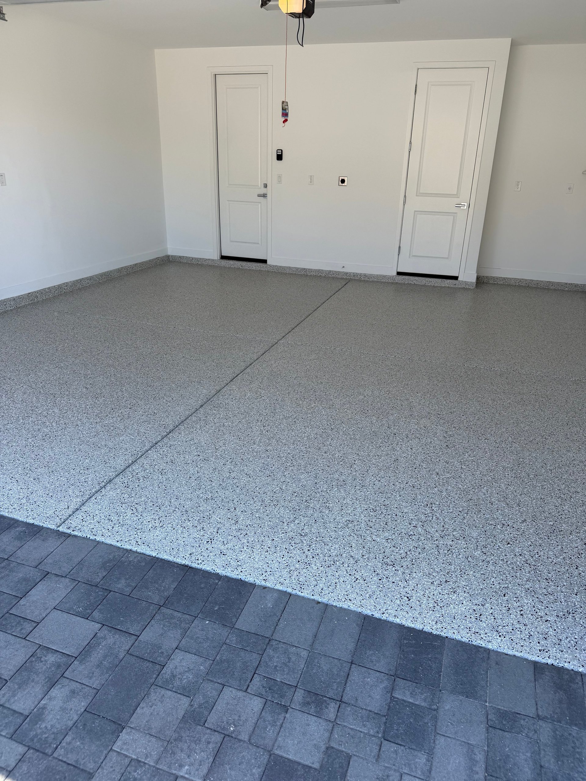 Empty garage interior with gray speckled epoxy flooring, white walls, and two white doors with hardware
