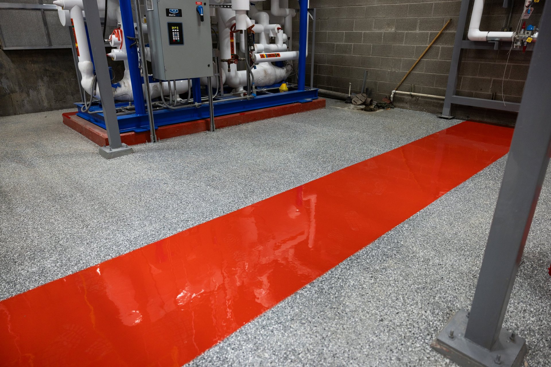 Industrial facility floor with bright red directional stripe and blue equipment platform on speckled gray concrete surface