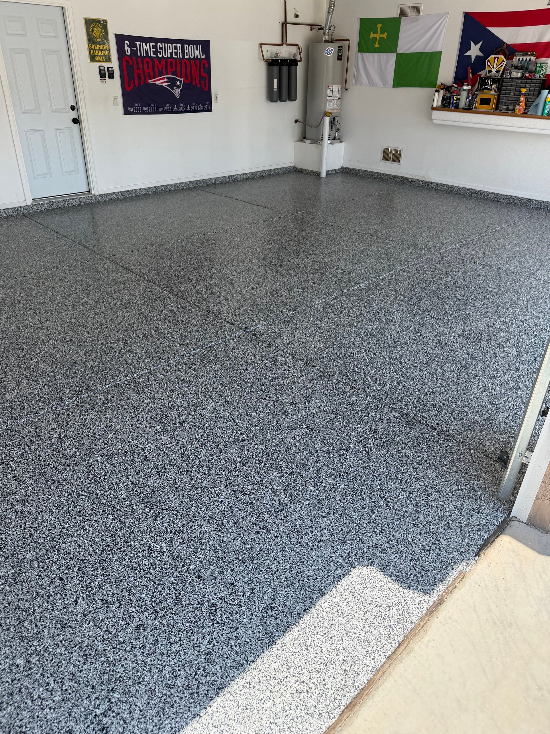 Empty garage interior with gray speckled epoxy floor, sports memorabilia on walls, and a white door