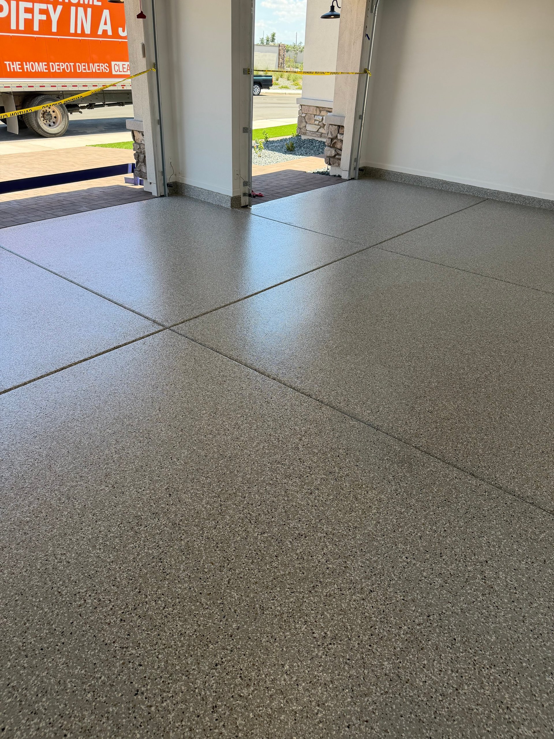 Interior of a garage or warehouse with polished concrete floor divided into sections, open garage door showing outdoor area with Home Depot truck visible