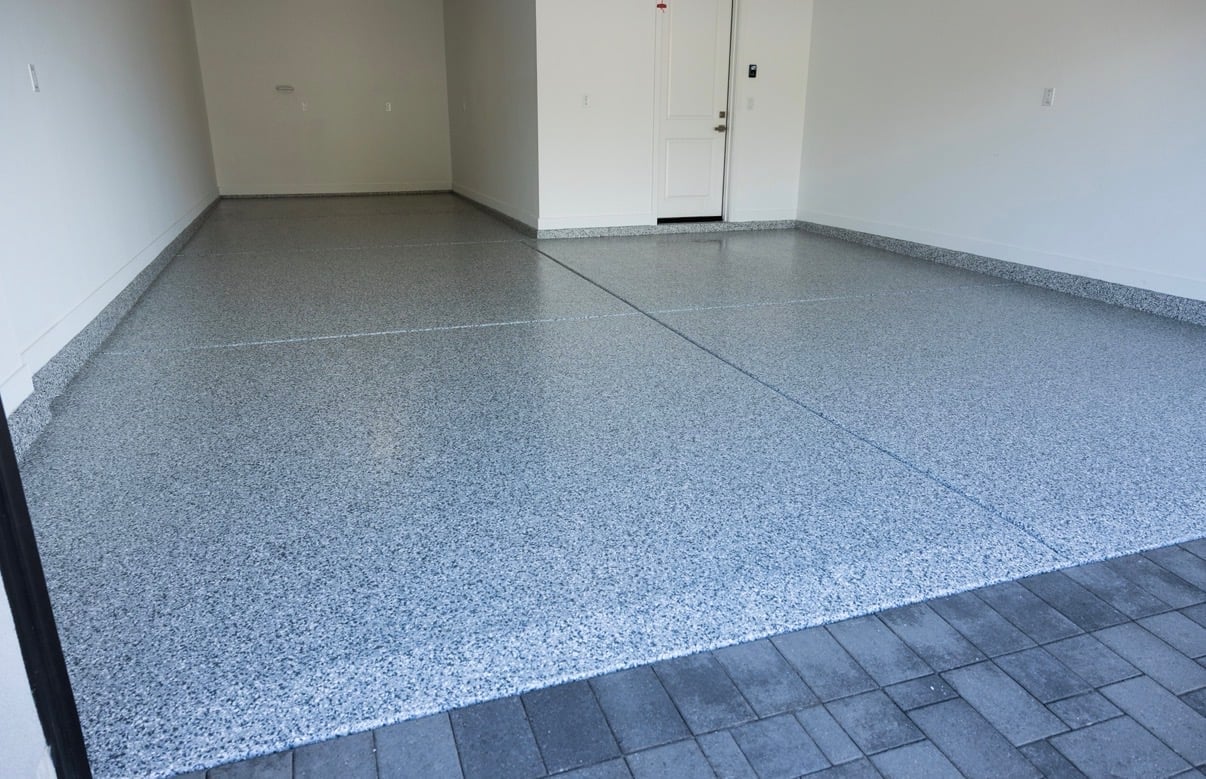 Empty garage interior with gray speckled epoxy floor, white walls, and closed door