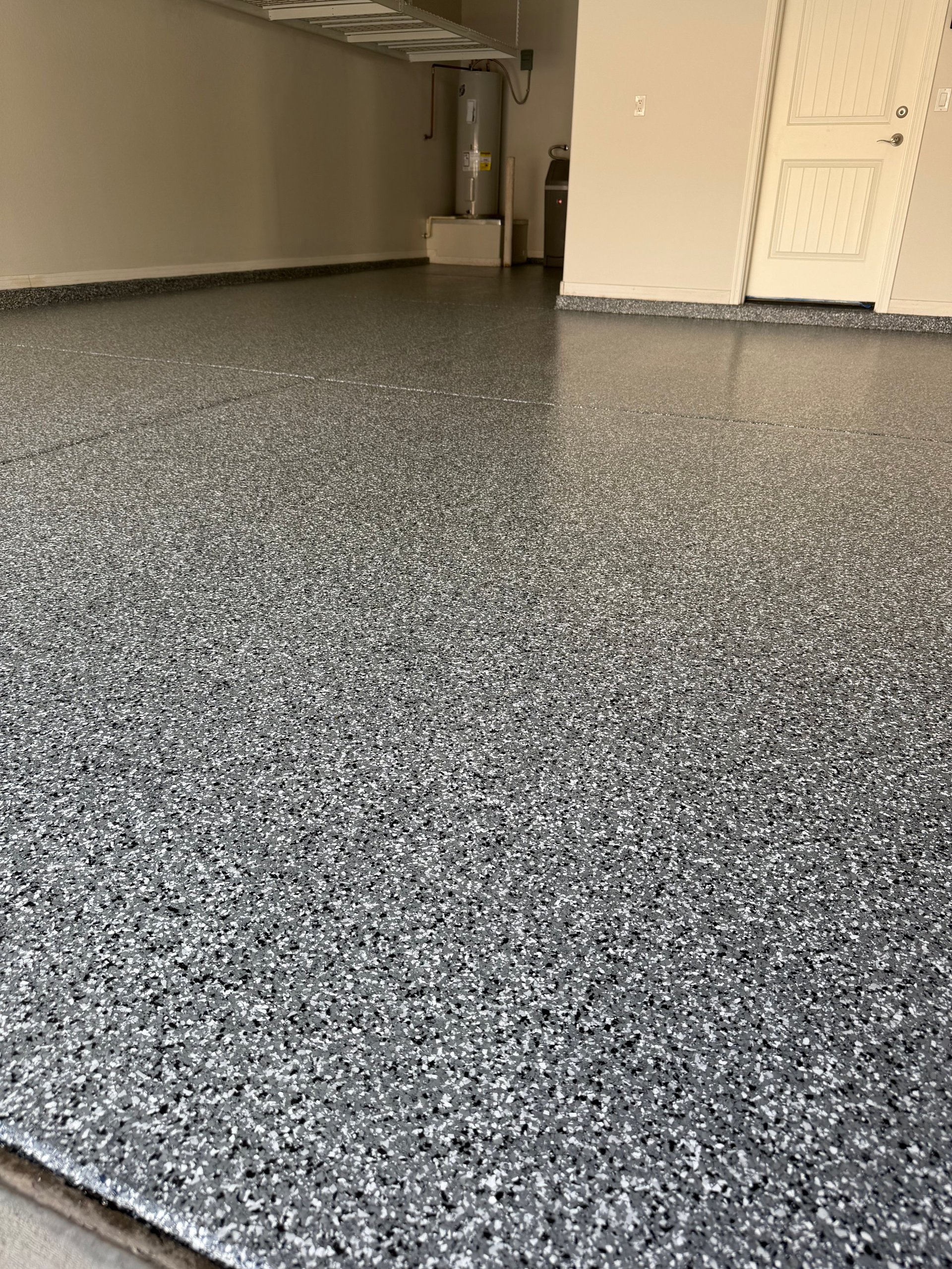 Spacious garage interior with gray speckled epoxy flooring, white door, and beige walls