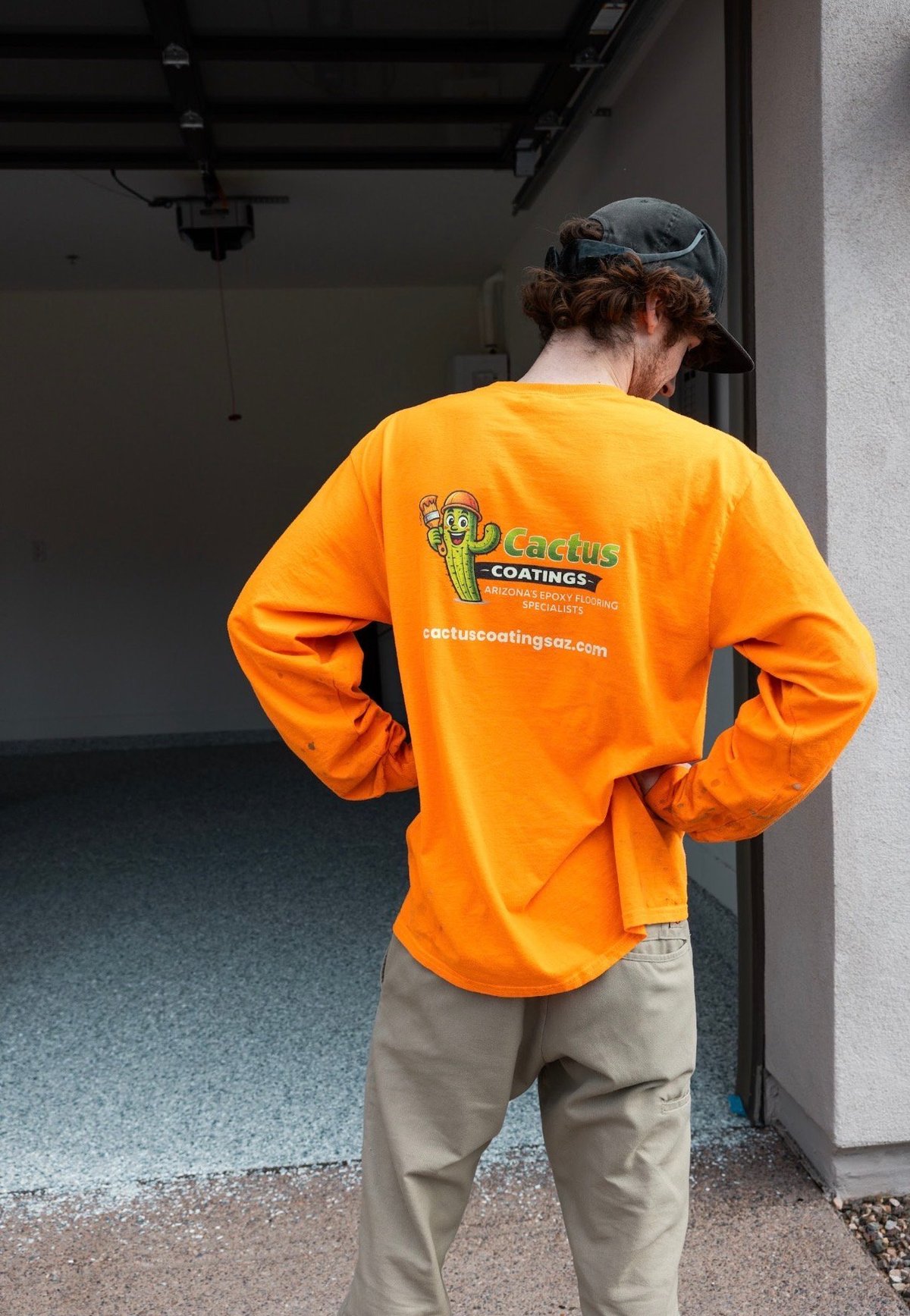 Person wearing orange Cactus Coatings work shirt and cap standing in industrial interior space