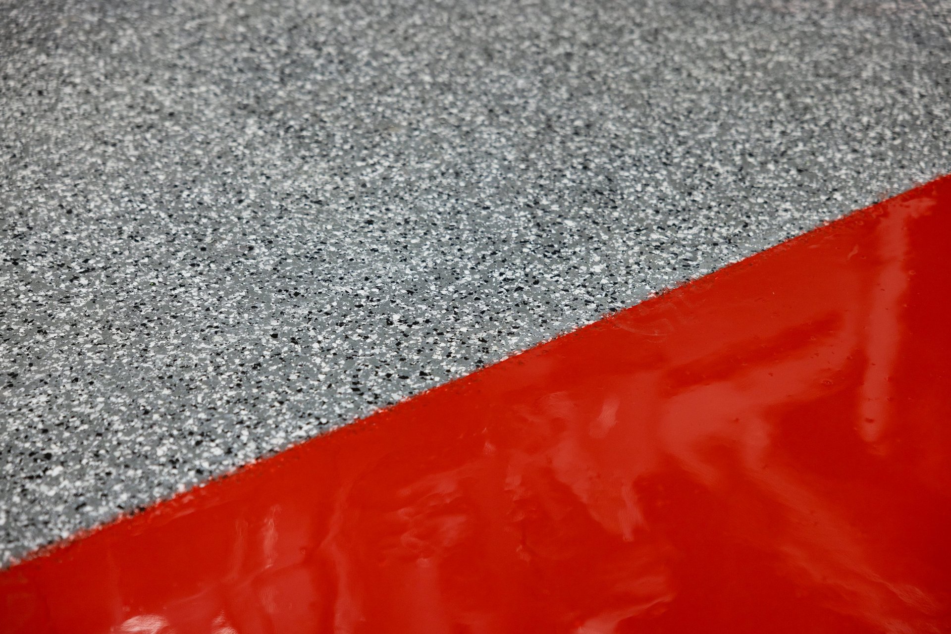 Close-up of gray speckled surface meeting red glossy material at a diagonal line