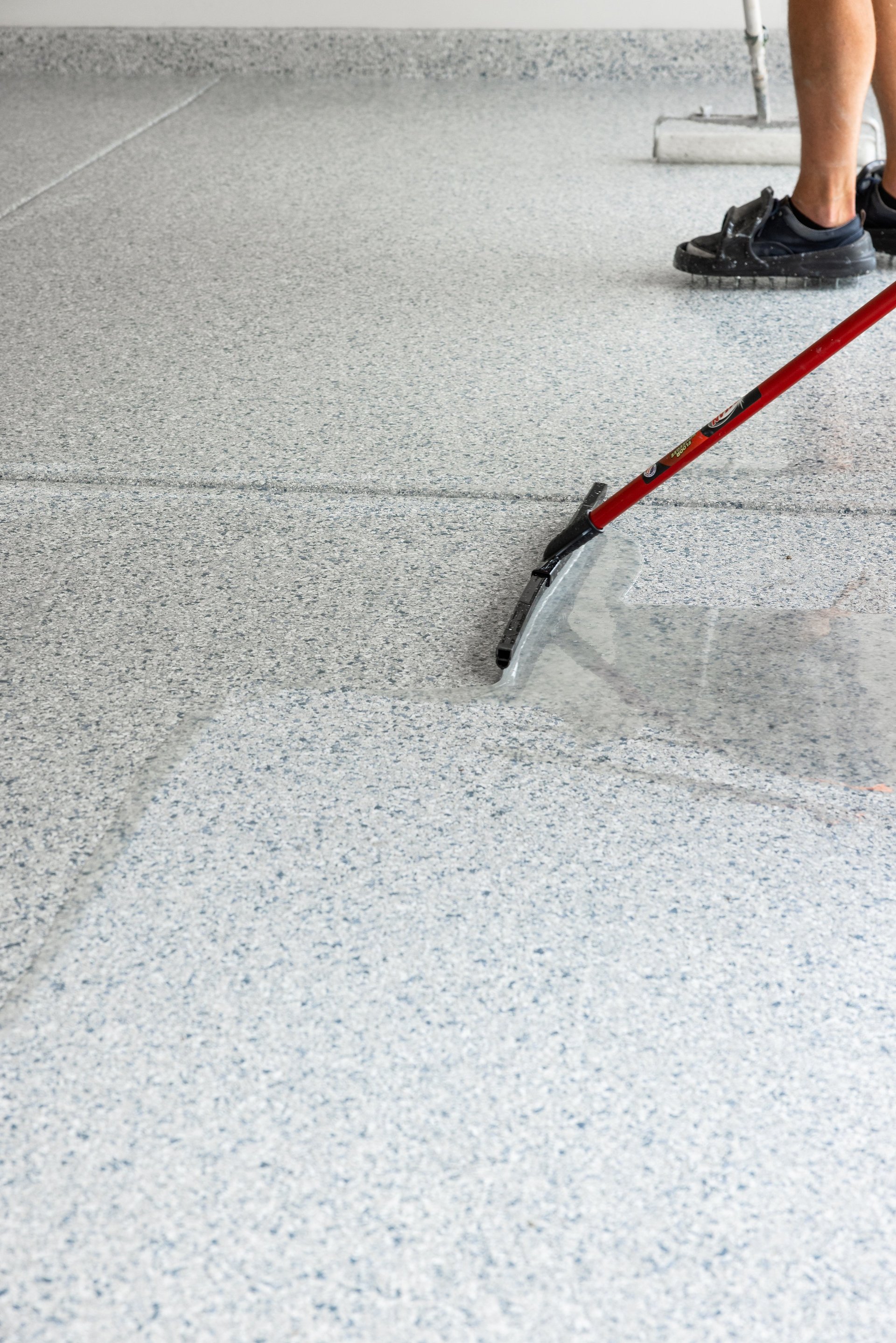 Worker applying epoxy coating to concrete floor with squeegee tool during resurfacing project