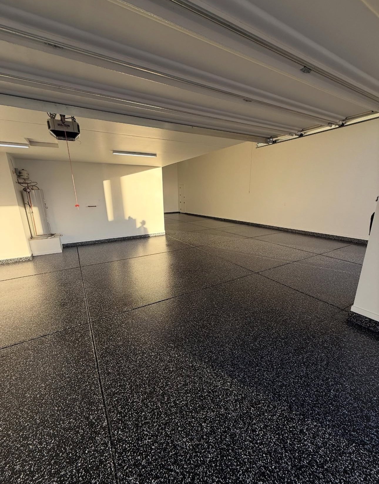 Empty modern garage interior with dark speckled epoxy flooring, white walls, and recessed ceiling lights