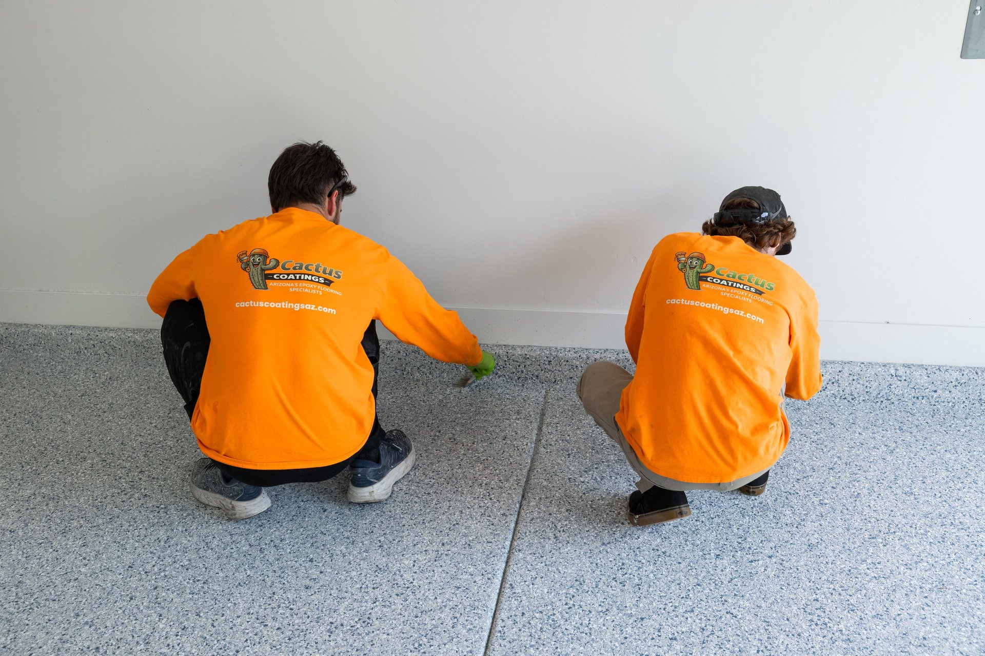 Two people wearing orange shirts and safety helmets crouching on a concrete floor