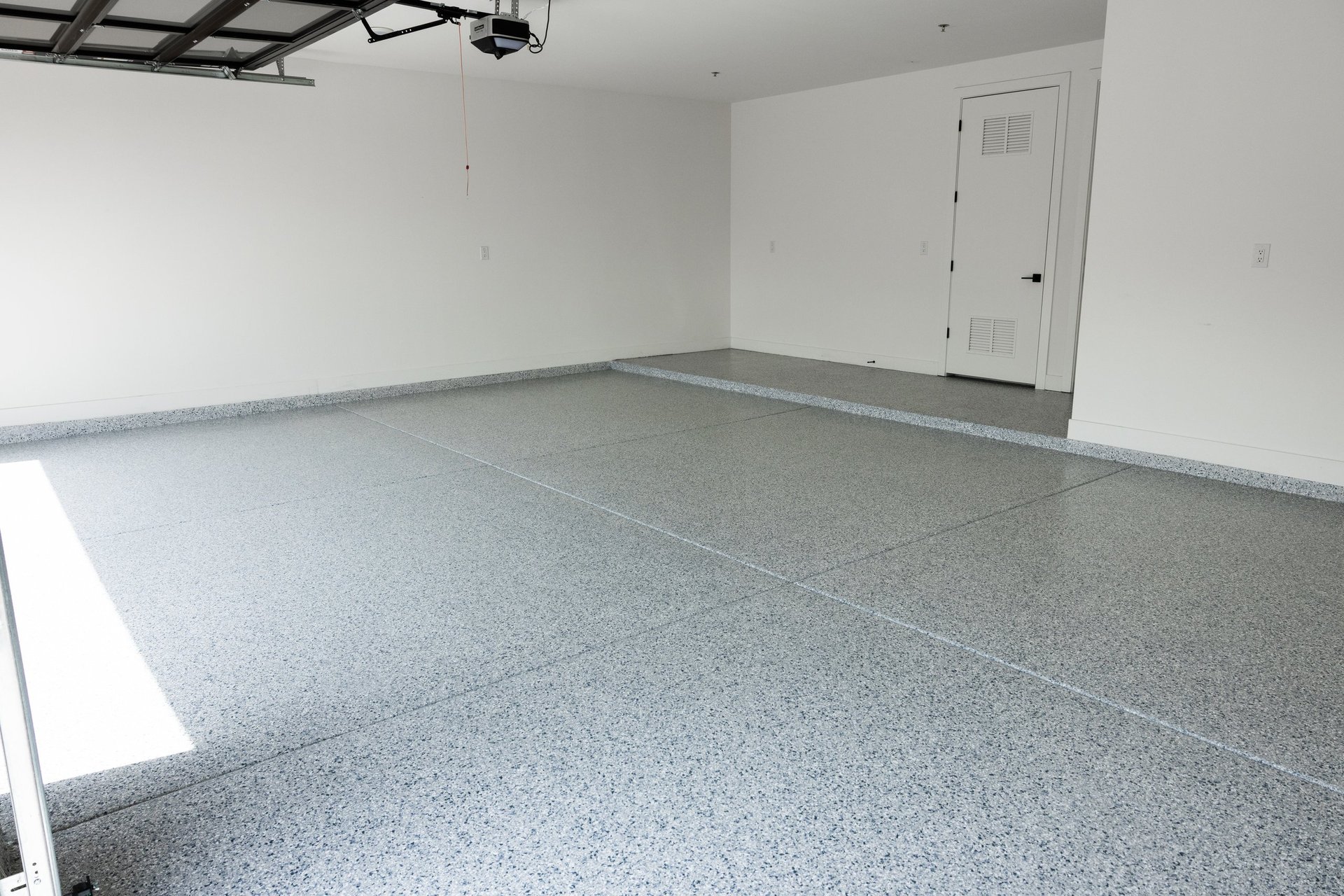Empty garage interior with gray epoxy flooring, white walls, overhead lighting, and a closed door