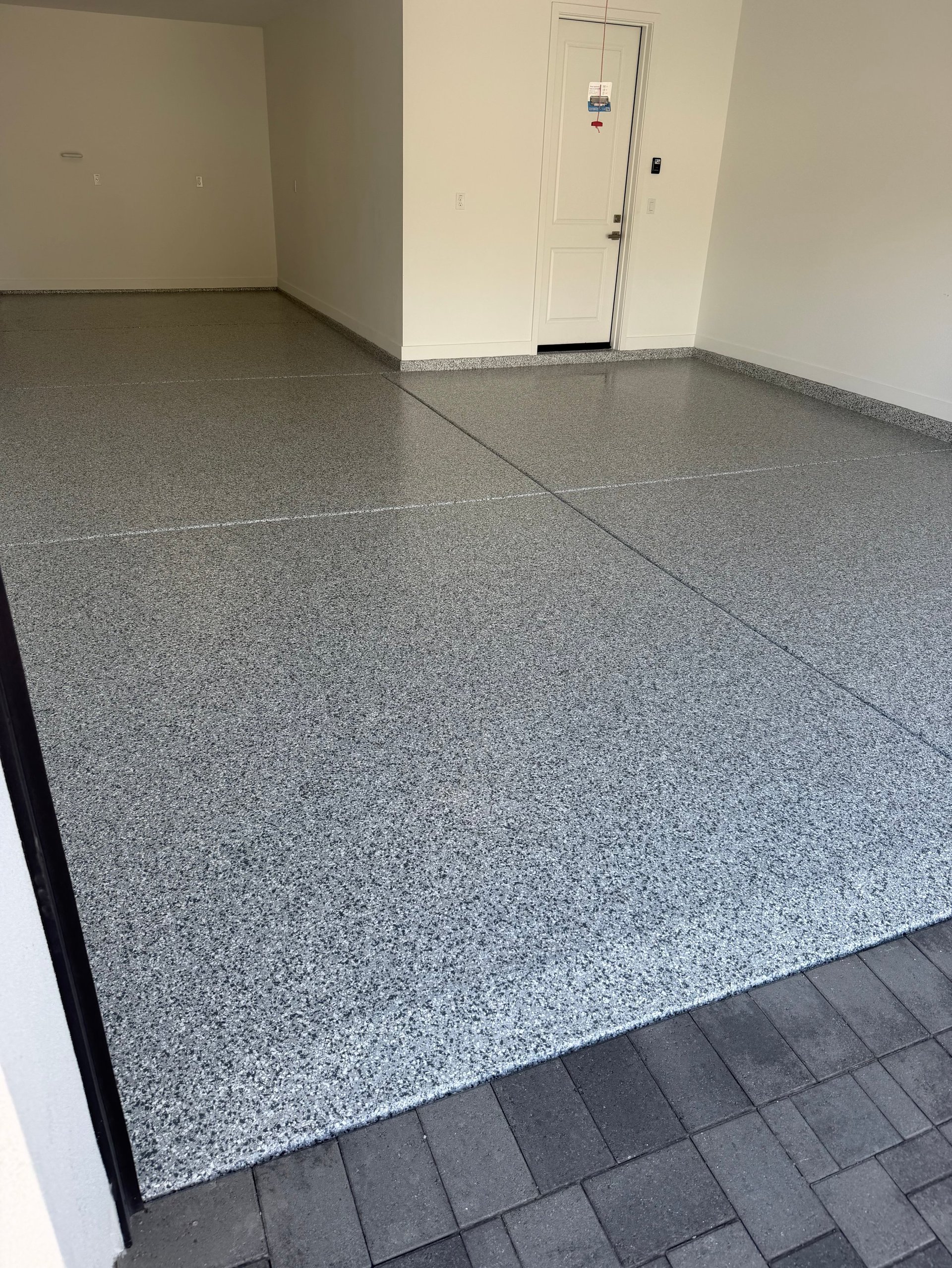Empty garage interior with gray speckled epoxy flooring, white walls, and white entry door