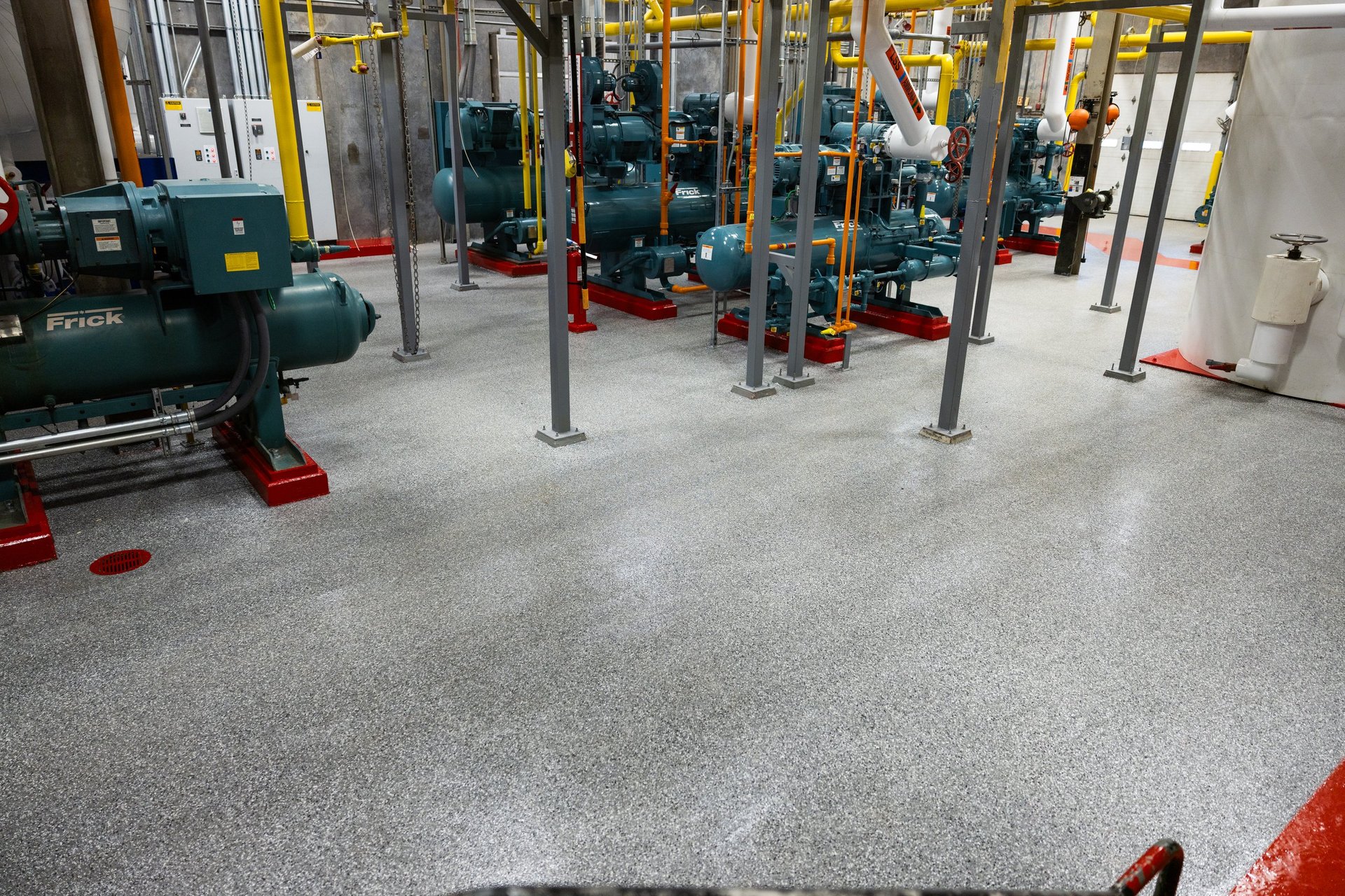 Industrial gym floor with exercise equipment, metal support columns, and red/pink markings on polished concrete