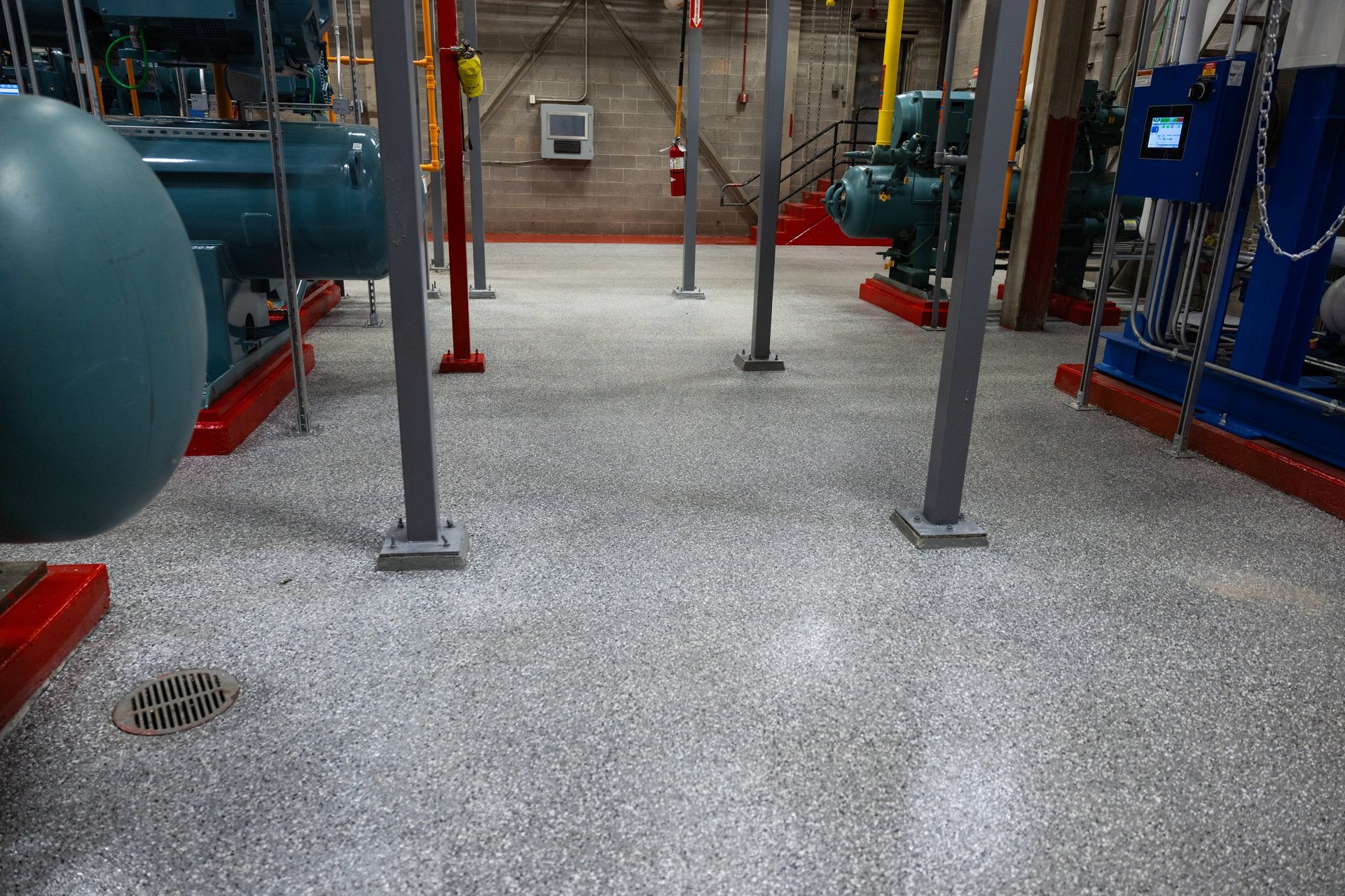 Modern automotive repair shop interior with gray epoxy flooring, support columns, red equipment, and industrial workspace