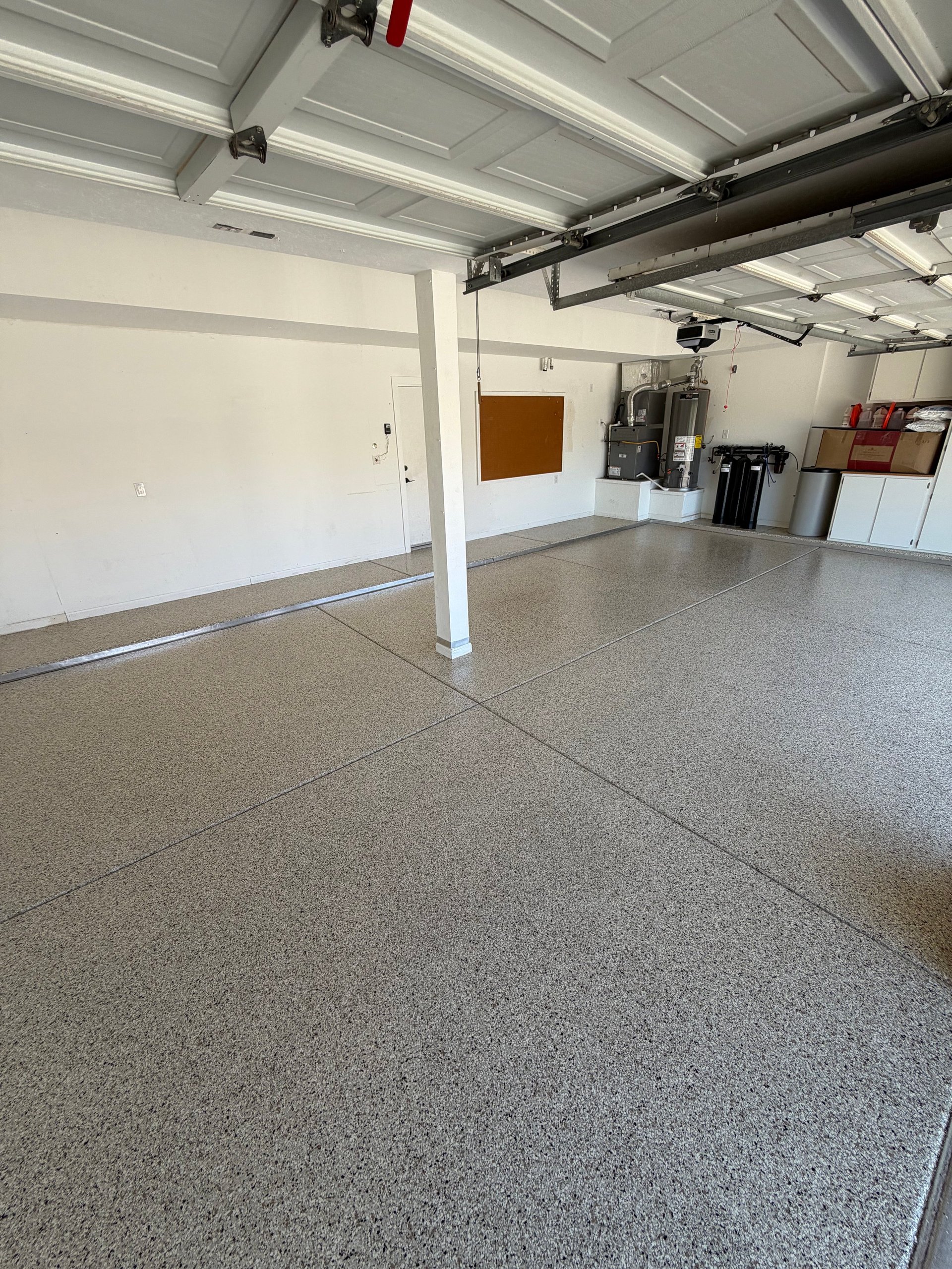 Empty garage interior with concrete floor, white walls, overhead door, and support column