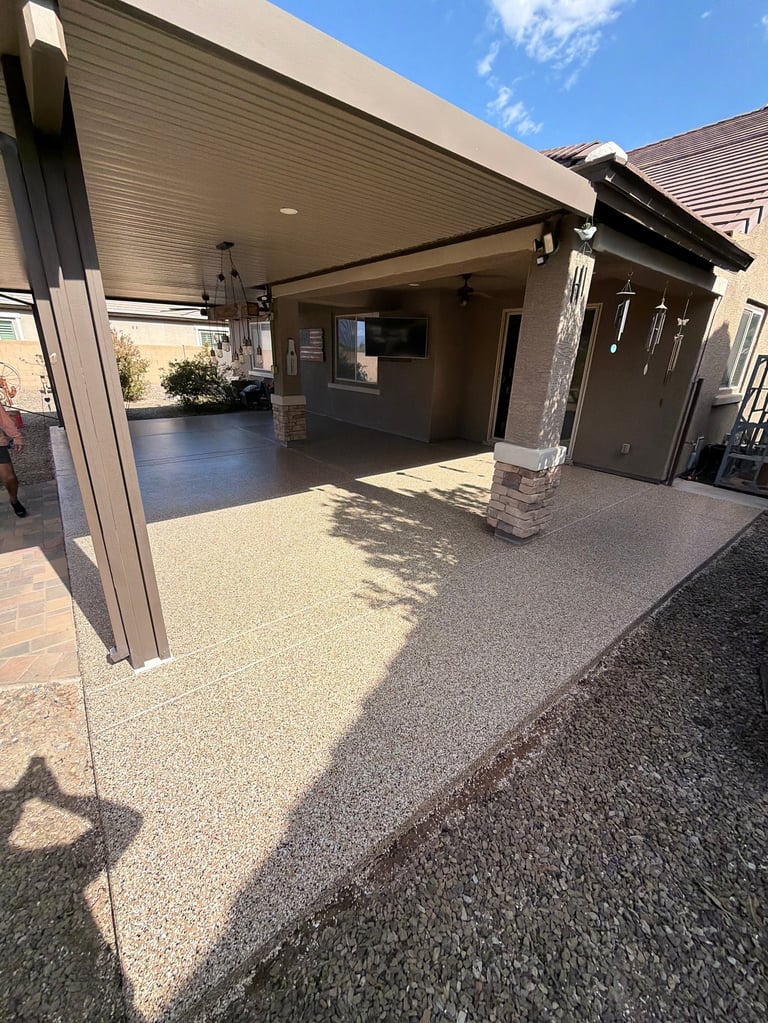 Modern residential garage with open patio area, concrete floor, and black garage door under clear blue sky