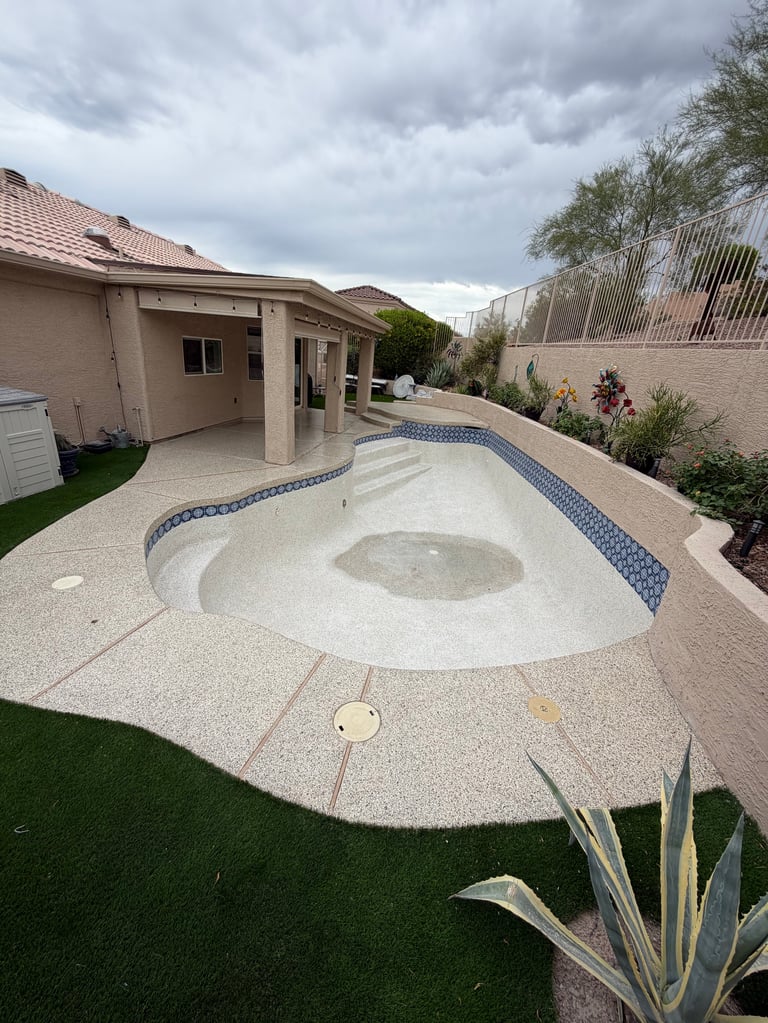 Backyard with empty drained swimming pool, patio, covered pergola, and landscaping under cloudy sky