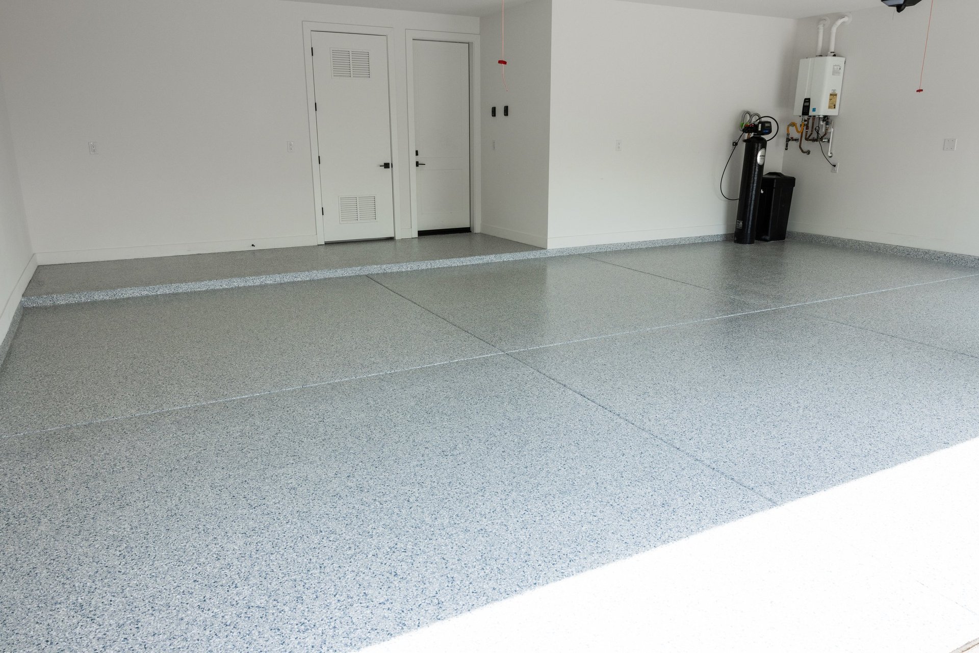 Clean empty garage interior with gray epoxy flooring, white walls, closed doors, and storage items against the wall