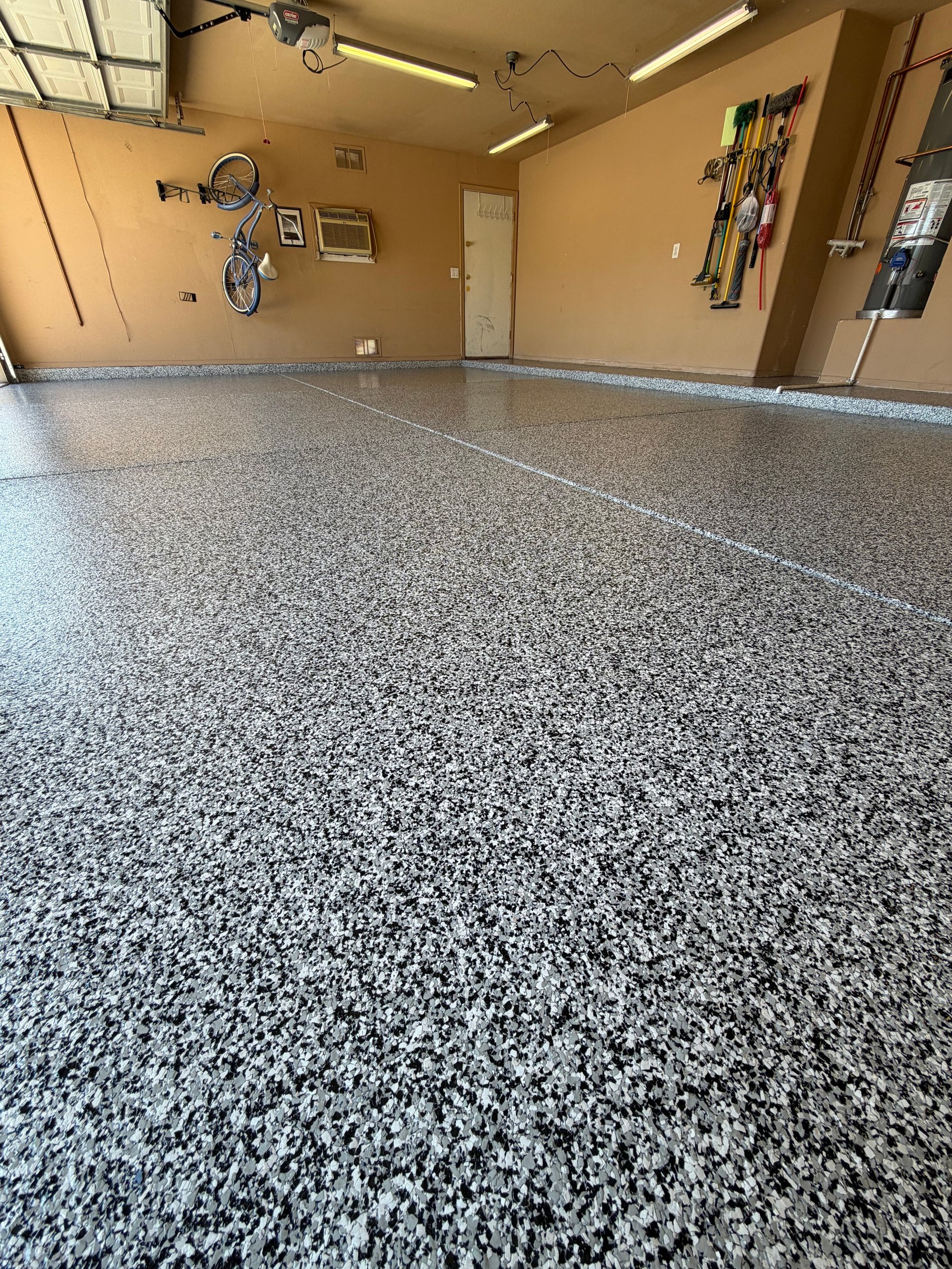 Clean garage interior with polished gray speckled epoxy floor, bike on wall, tools on pegboard, and beige walls