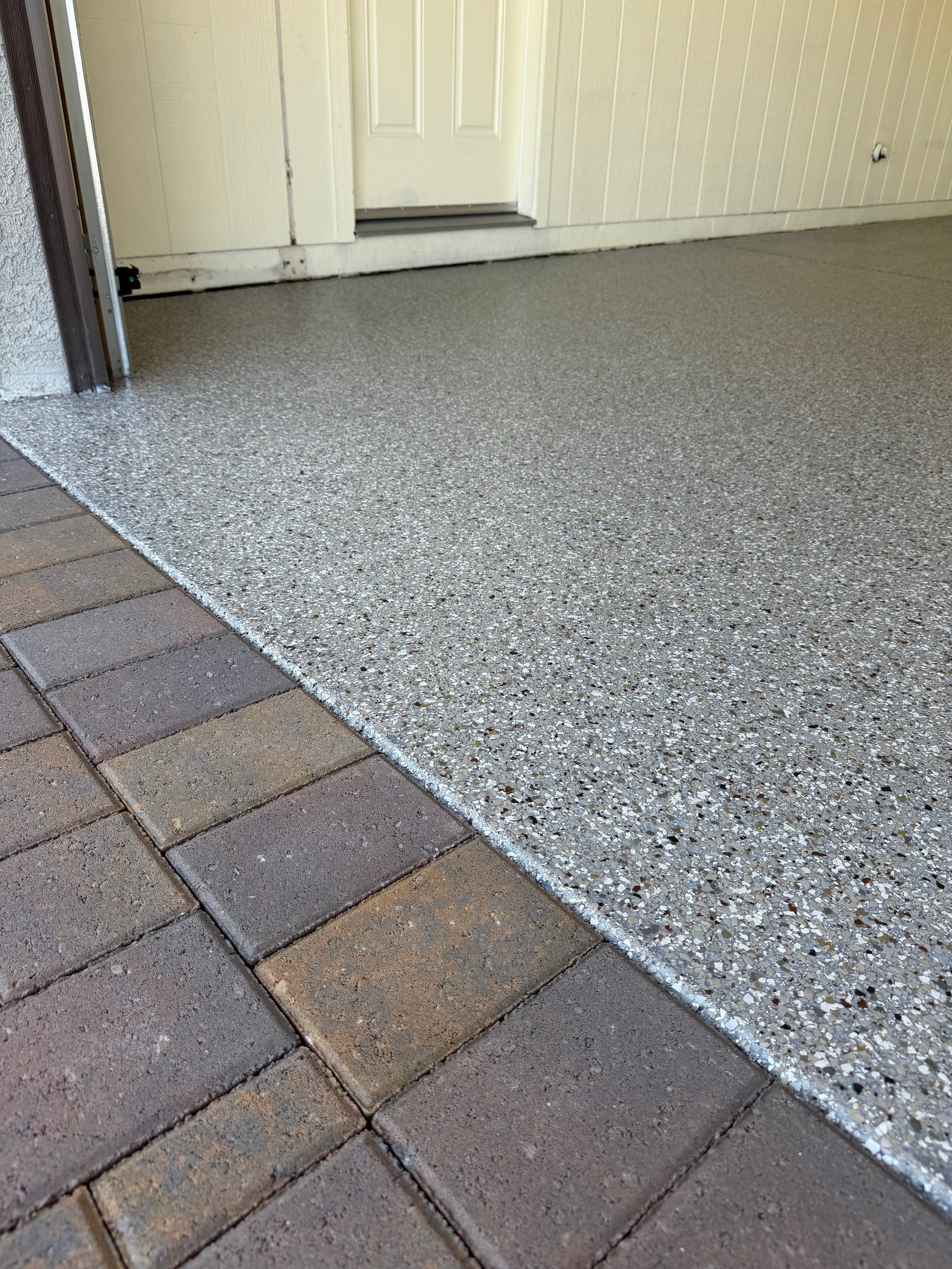 Garage entryway showing transition between brown paver flooring and gray speckled epoxy flooring with white paneled garage door