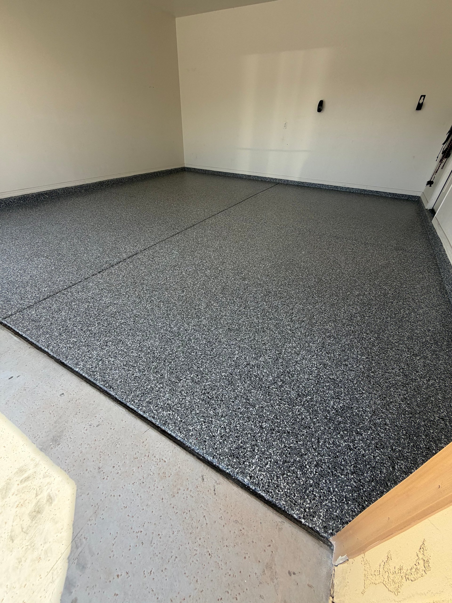 Empty garage or storage room with gray speckled epoxy flooring installed over concrete, white walls, and a light switch visible