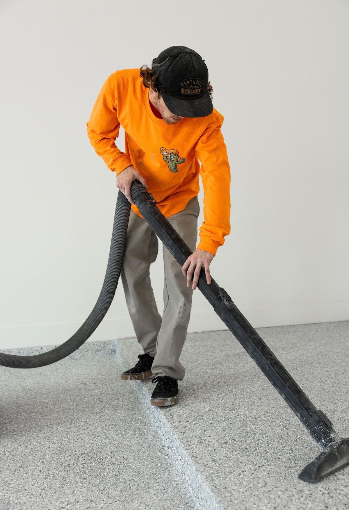 Person in orange hoodie and black cap using a pressure washer to clean a concrete floor