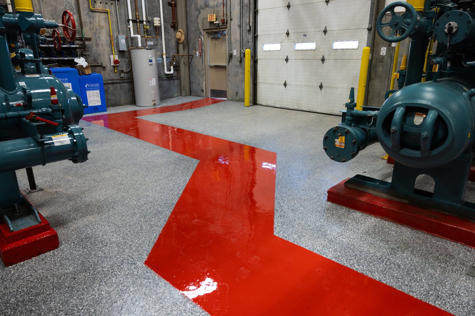 Red directional arrow painted on gray workshop floor with industrial equipment and machinery in background